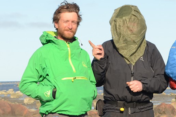 Man with mosquito headnet pointing at another man without headnet